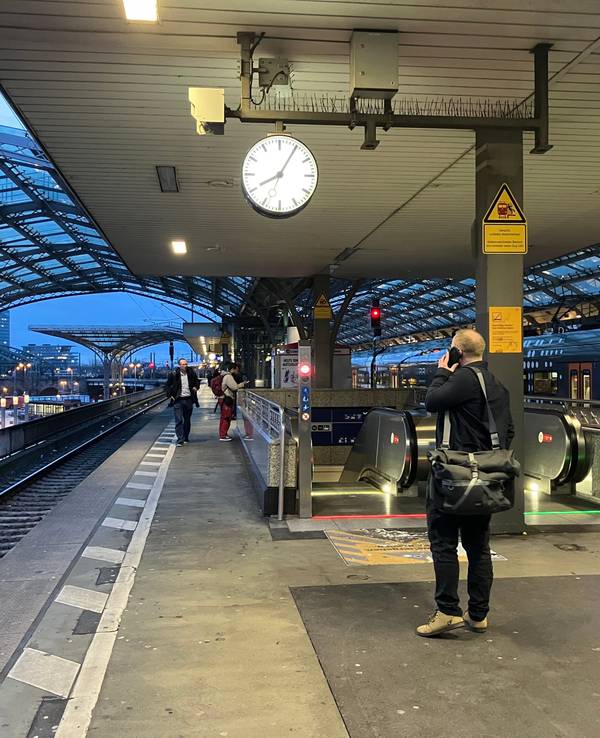 Foto von einem Bahnsteig am Kölner Hauptbahnhof, im Vordergrund ist ein Mann zu sehen, der mit dem Handy telefoniert.