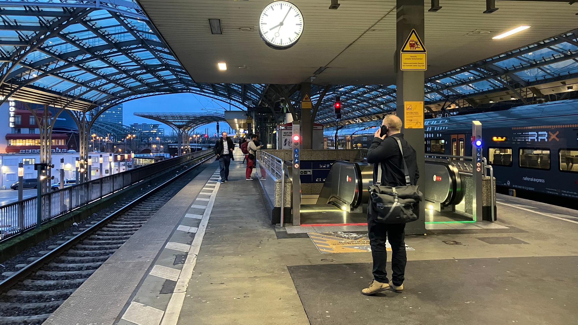 Foto von einem Bahnsteig am Kölner Hauptbahnhof, im Vordergrund ist ein Mann zu sehen, der mit dem Handy telefoniert.