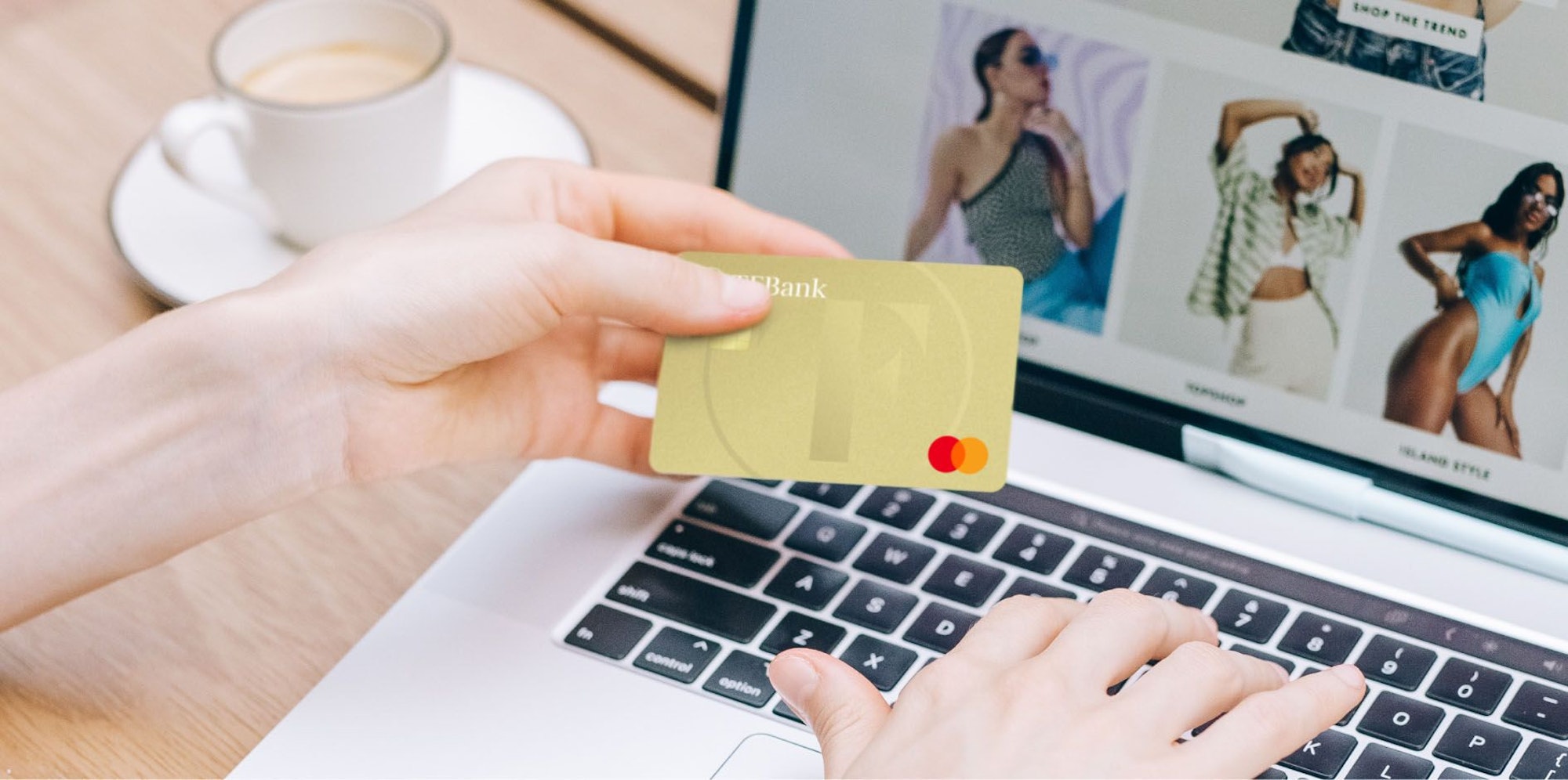 Eine weibliche Hand hält die Kreditkarte TF Mastercard Gold. Die andere Hand tippt etwas in den Laptop.