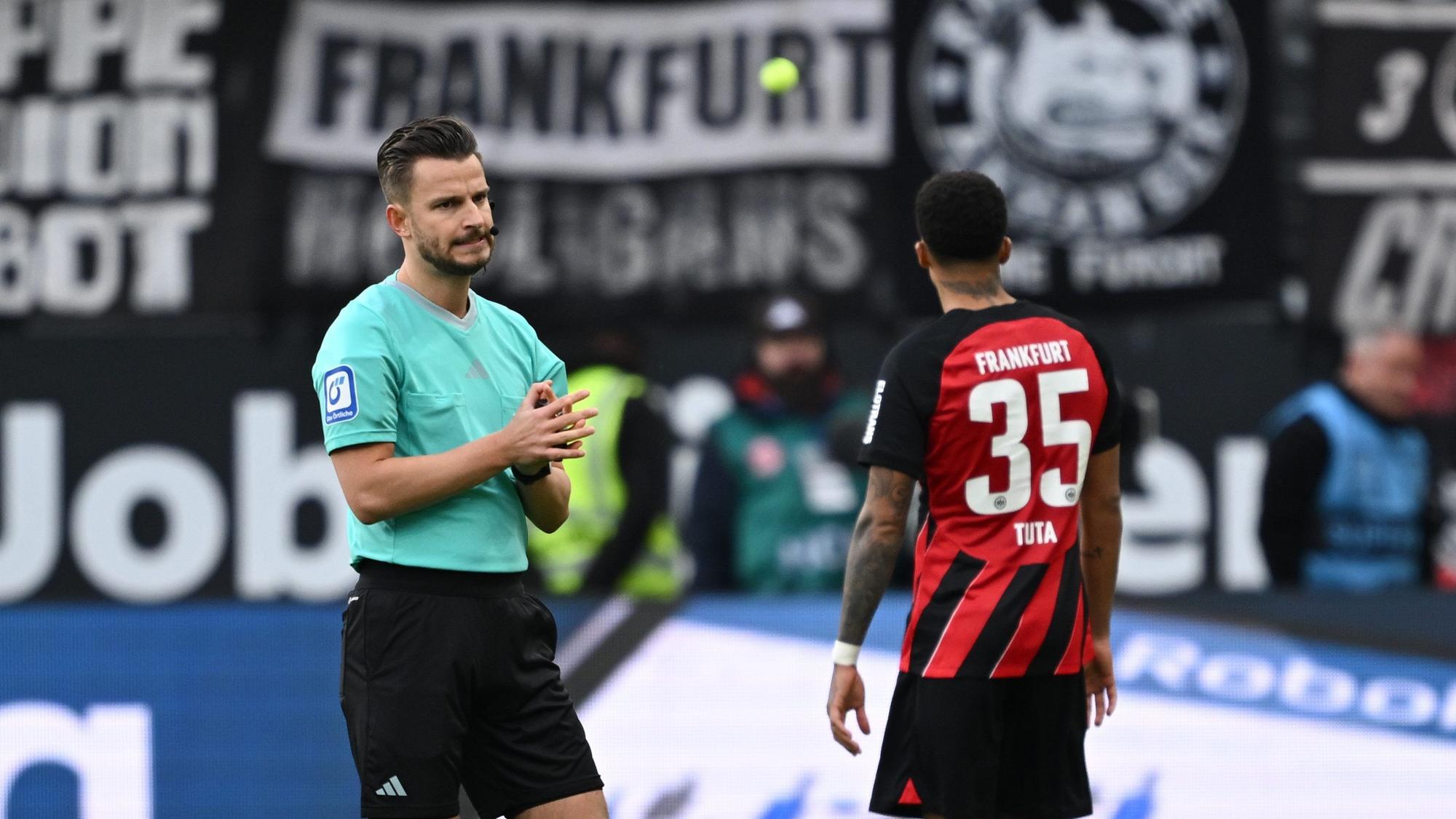 Tennisbälle aus dem Frankfurter Fanblock fliegen vor Schiedsrichter Daniel Schlager (l.) und Frankfurts Tuta auf den Platz.