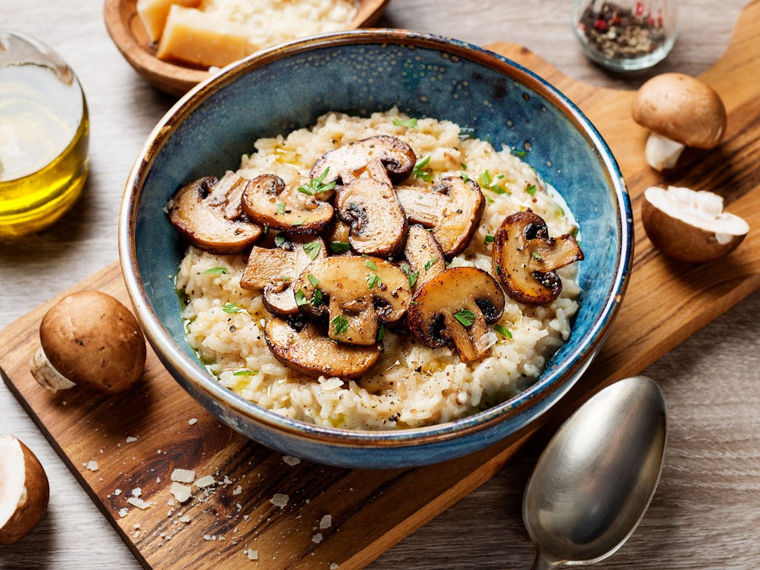 Risotto mit braunen Pilzen ist mit einem Teller auf einem Holzbrett angerichtet