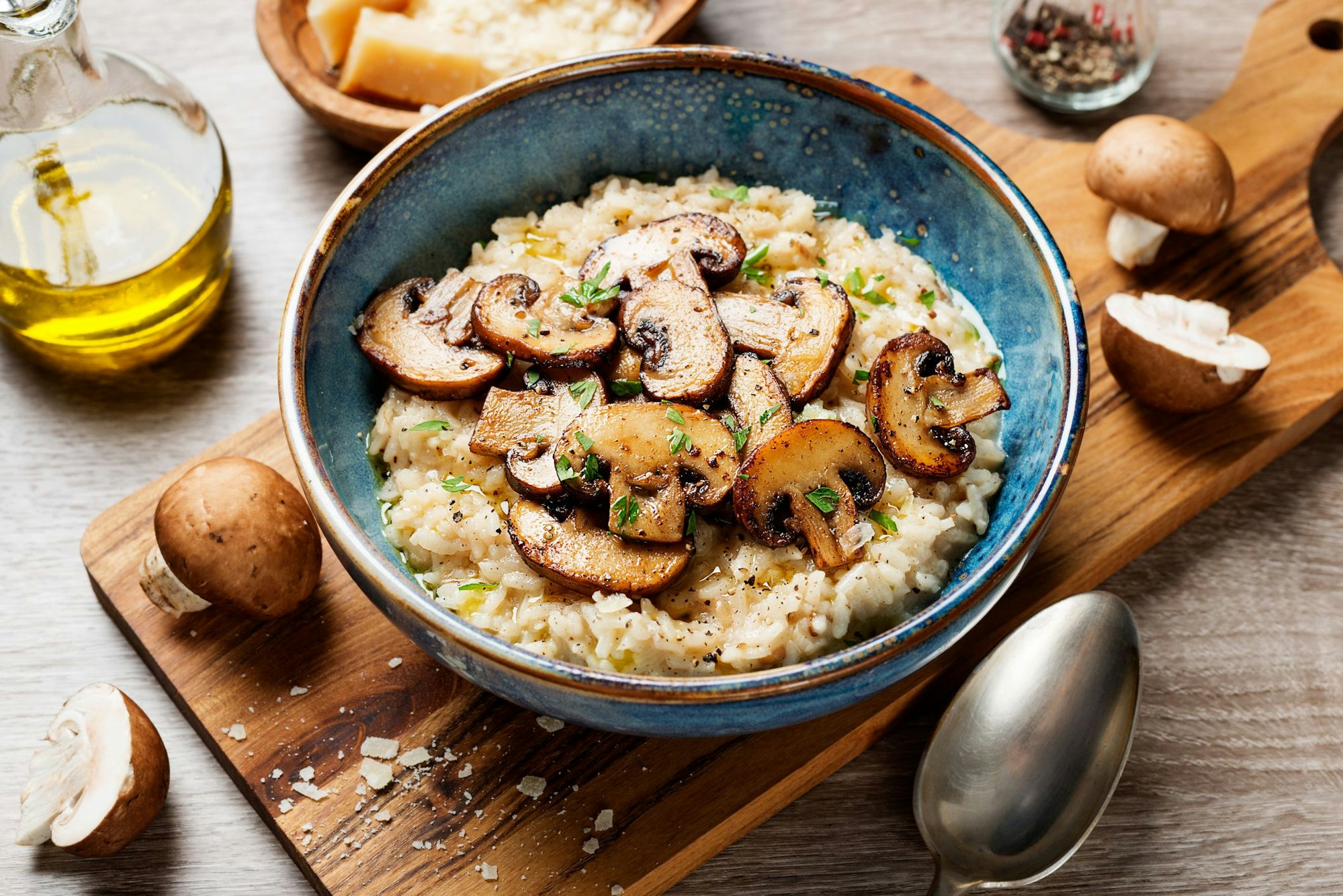 Risotto mit braunen Pilzen ist mit einem Teller auf einem Holzbrett angerichtet