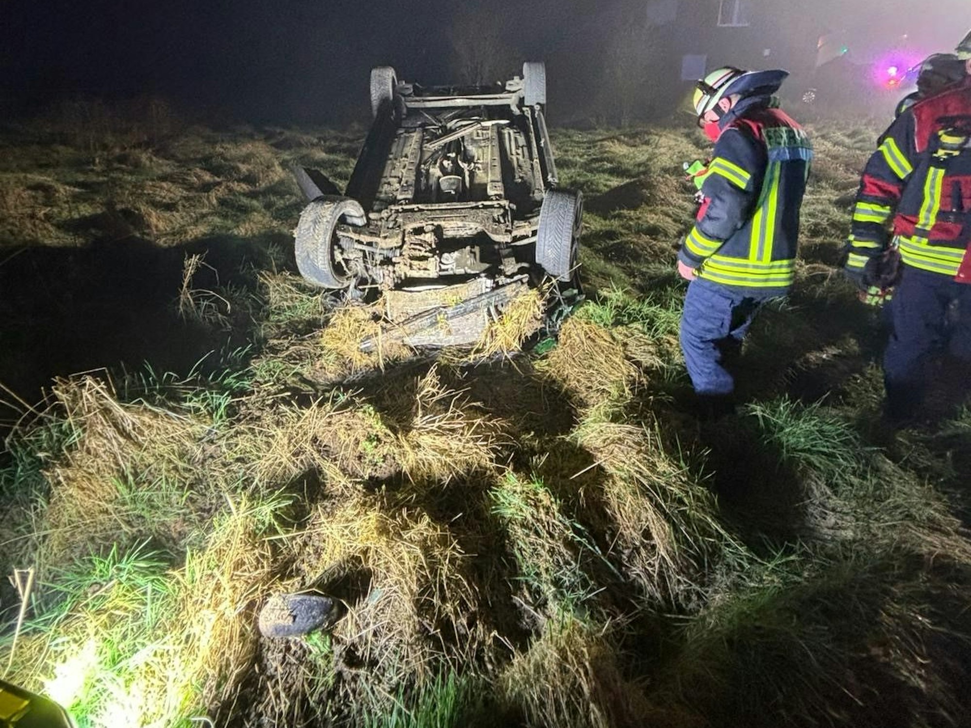 Ein Auto liegt auf dem Dach auf einer stark beschädigten Wiese.