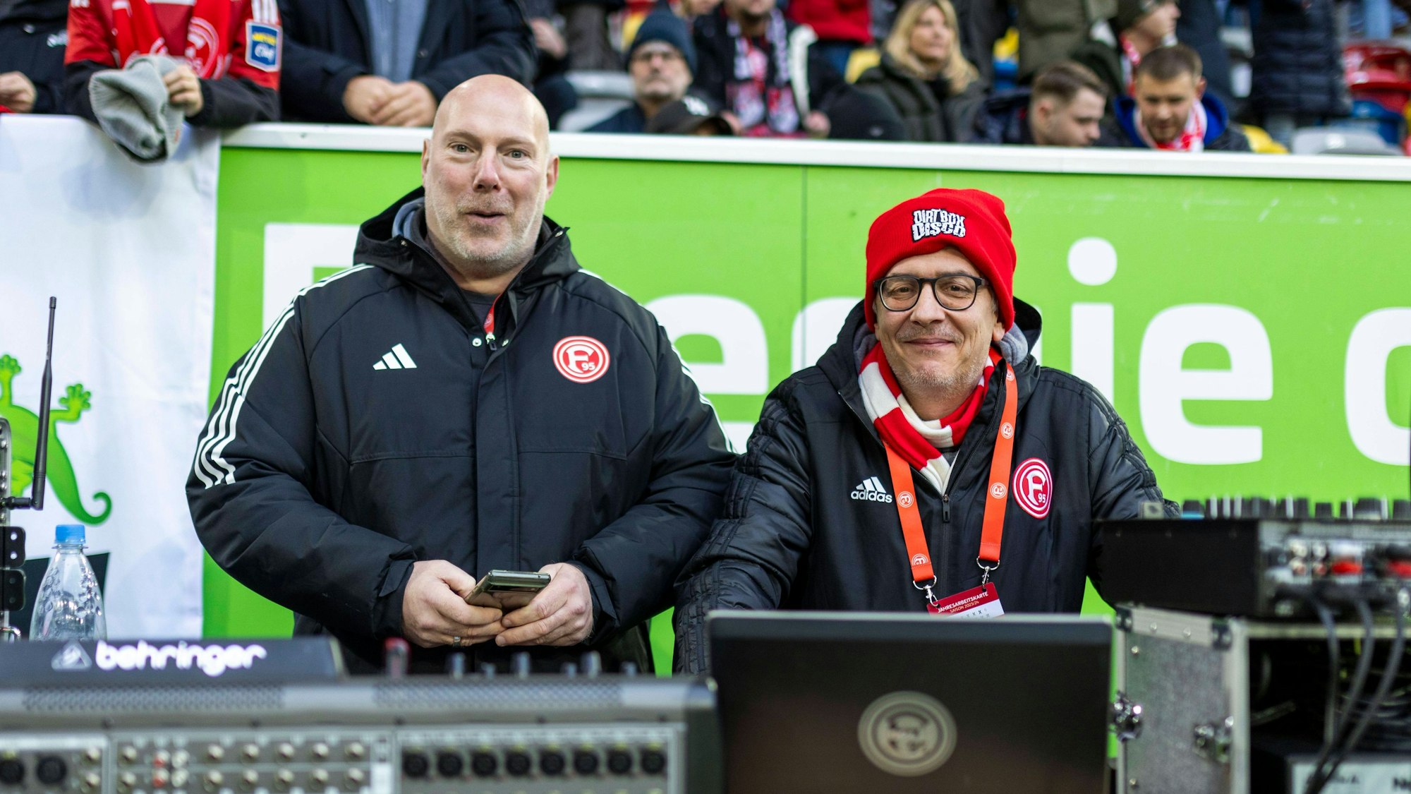 Fortuna Düsseldorfs Stadion-DJ Marcus „Opa“ Haefs und Techniker Carsten Johns lächeln beim Heimspiel gegen Holstein Kiel in die Kamera.