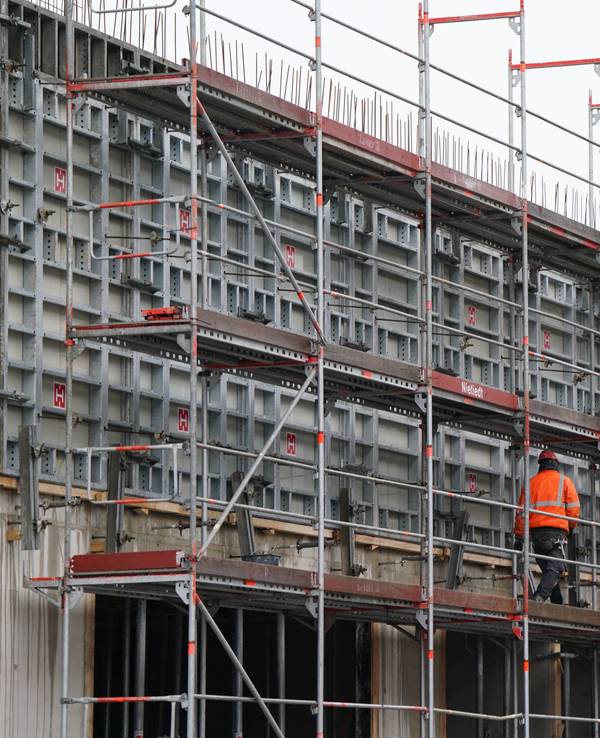 Ein Bauarbeiter geht über ein Baugerüst auf einer Baustelle.