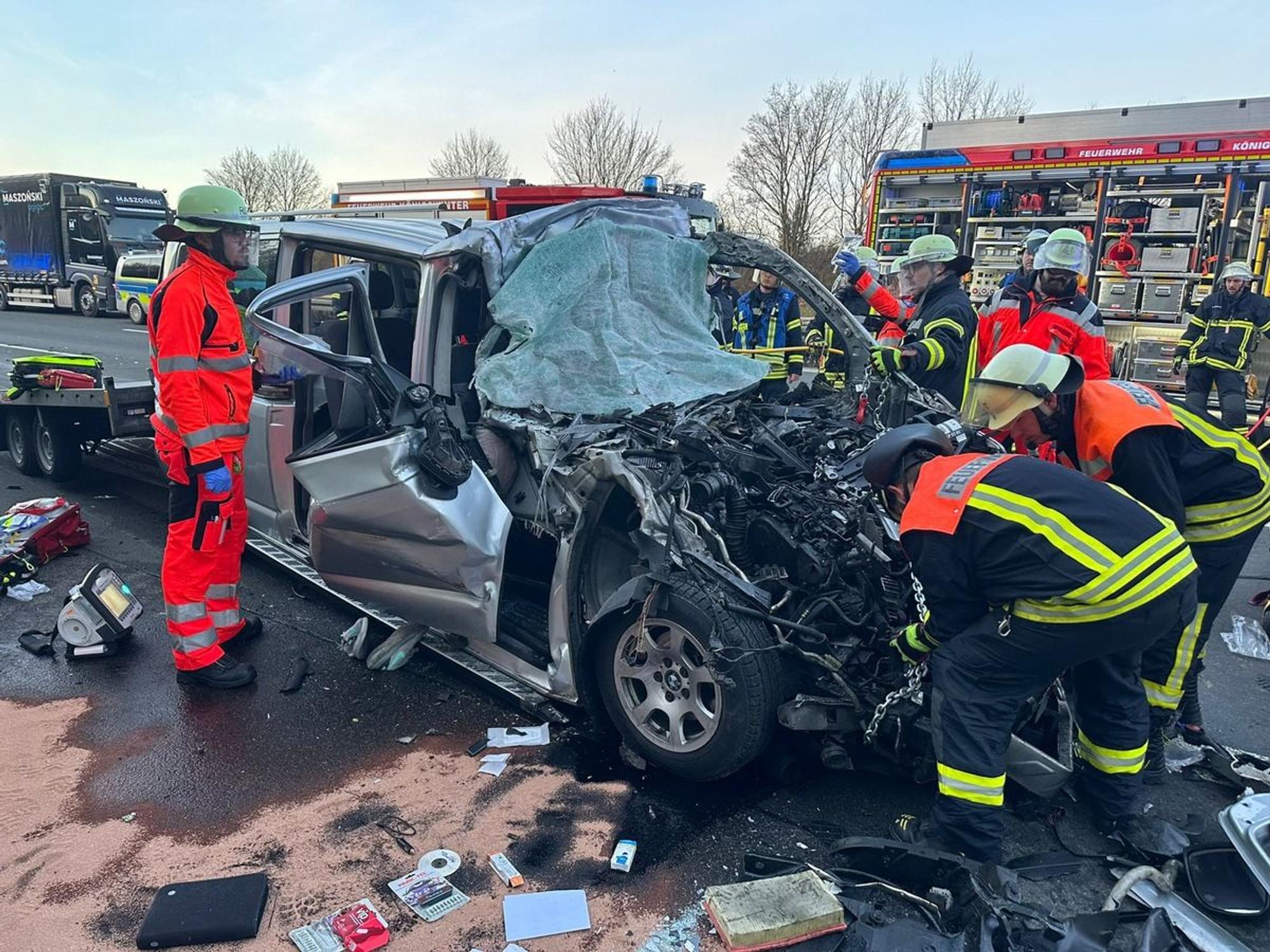 Ein deformierter Transporter steht inmitten von Trümmerteilen auf der Fahrbahn, mehrere Einsatzkräfte der Feuerwehr machen sich an ihm zu schaffen.