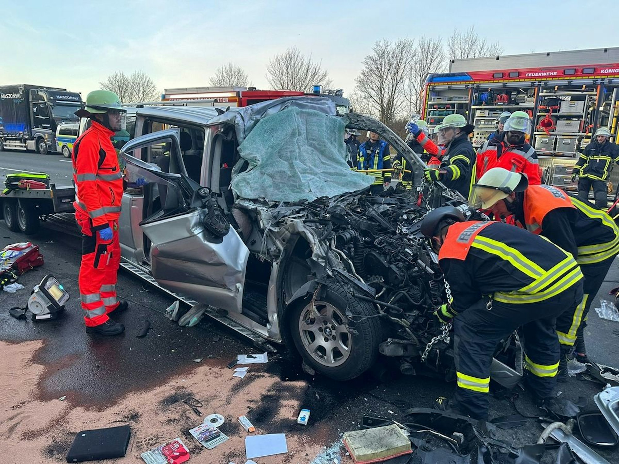 Ein deformierter Transporter steht inmitten von Trümmerteilen auf der Fahrbahn, mehrere Einsatzkräfte der Feuerwehr machen sich an ihm zu schaffen.