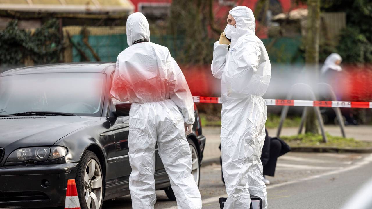 Zwei Kräfte der Spurensicherung stehen neben einem Auto, wenige Meter entfernt hat die Polizei den Bereich mit Flatterband abgesperrt.