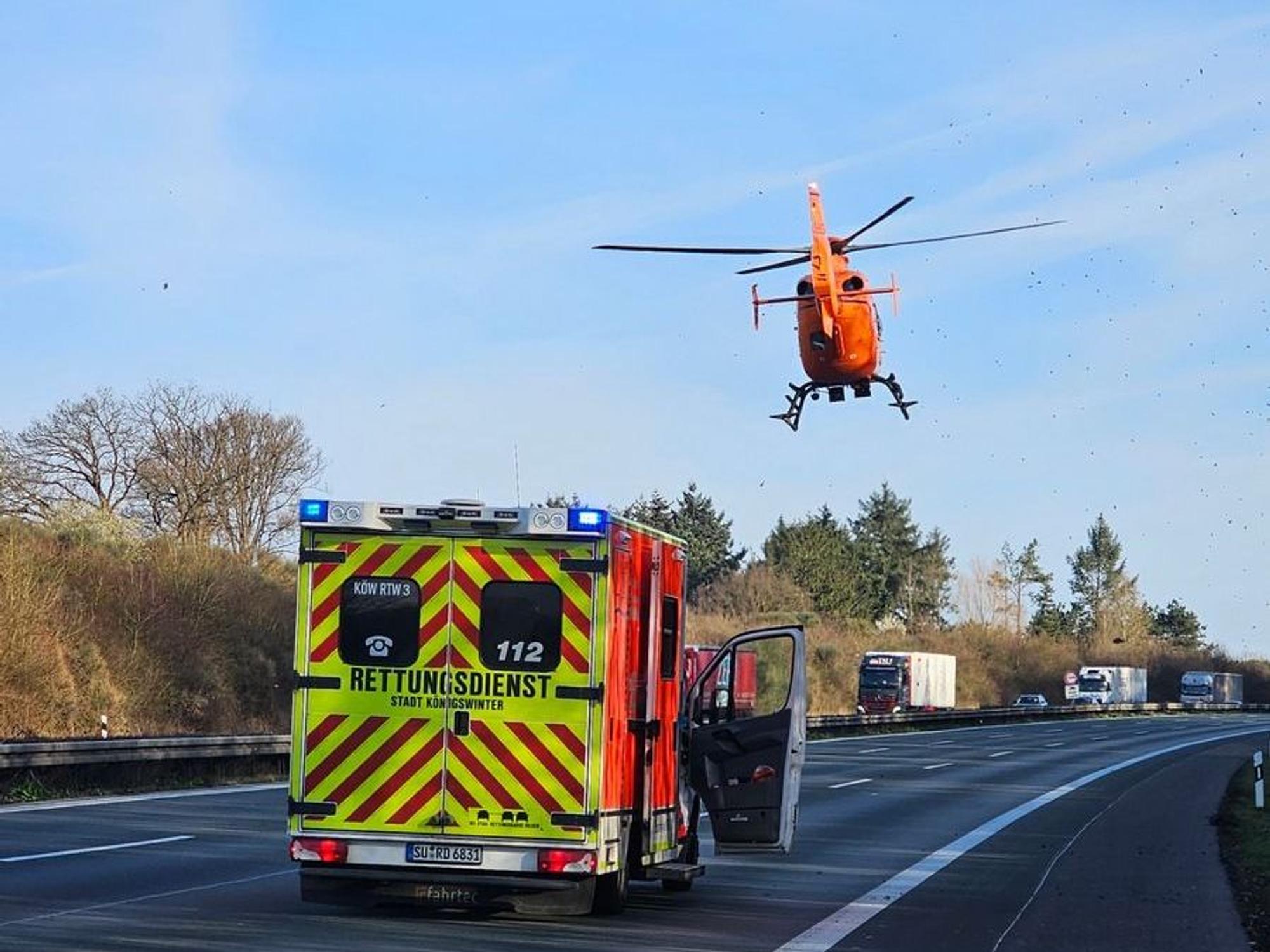 Ein Rettungshubschrauber ist über einer leeren Autobahn in der Luft, auf der Autobahn steht ein Rettungsfahrzeug.
