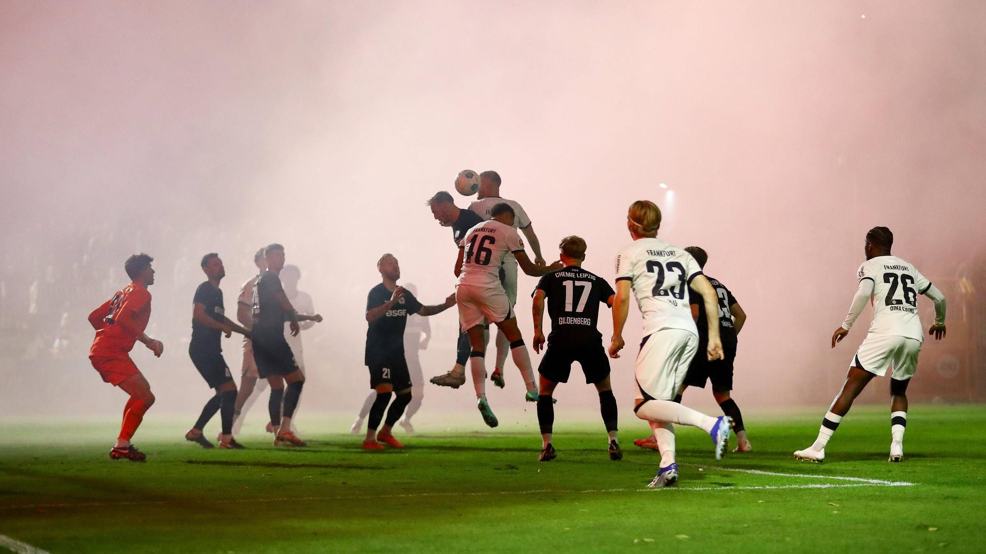 Spieler von Chemie Leipzig und Eintracht Frankfurt im dichten Rauch.