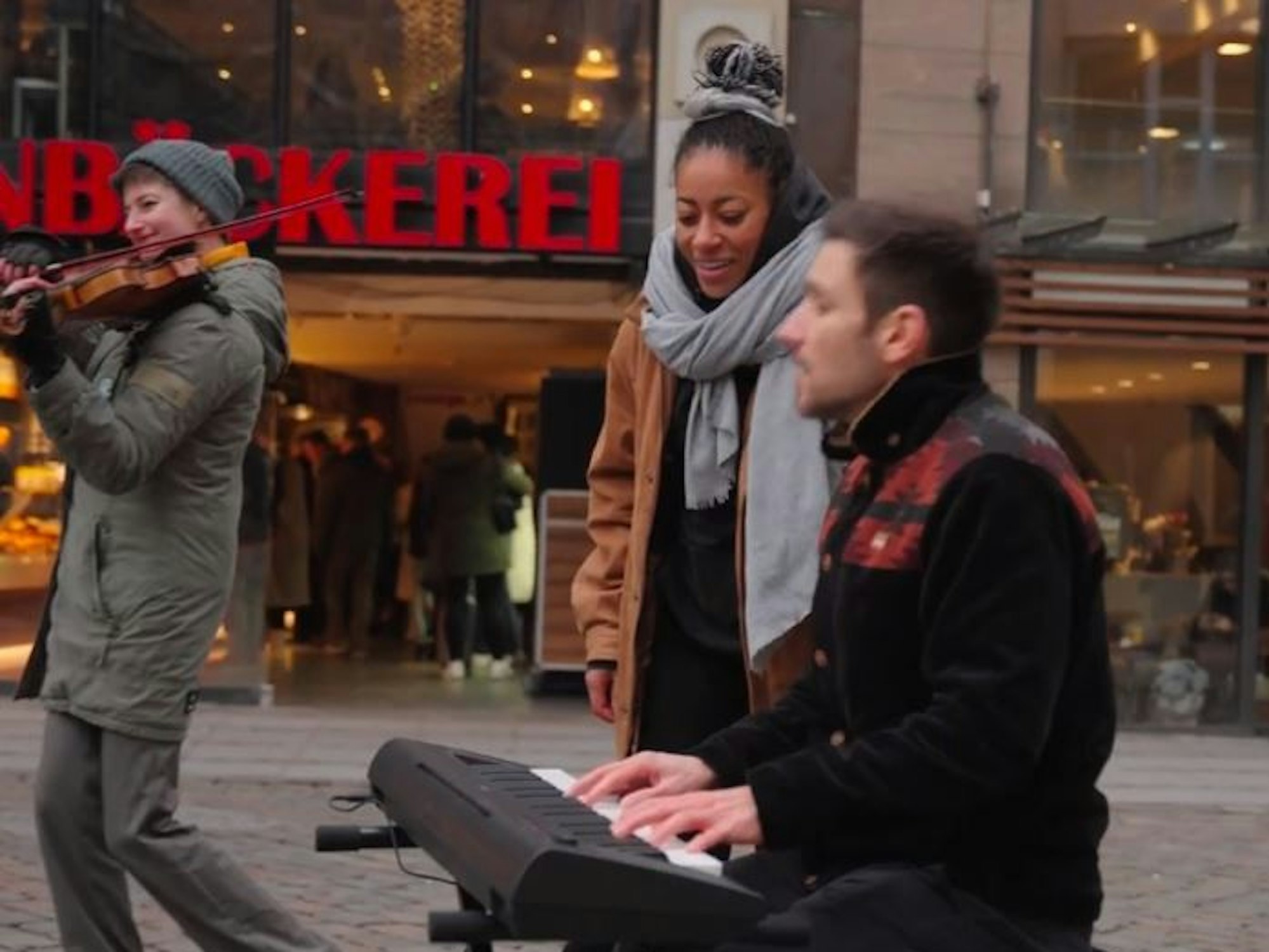 Der Kölner Sänger Julian Adler, Sängerin Diana Ezerex und Violinistin Felicitas Fischbein spielen auf einem Platz in Hamburg.