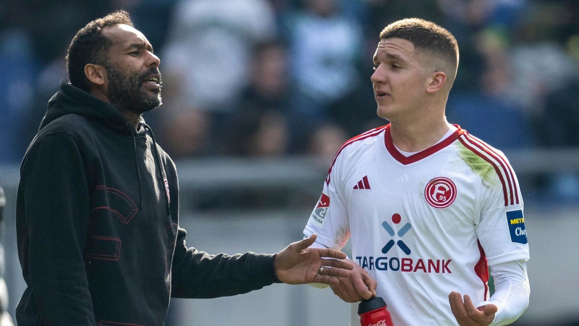 Fortuna Düsseldorfs Trainer Daniel Thioune und Doppeltorschütze Christos Tzolis sprechen auf dem Platz.