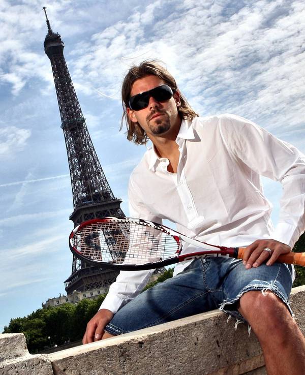 Daniel Köllerer posiert in Jeans-Shorts, weißem Hemd und Tennisschläger vor dem Eiffelturm in Paris.