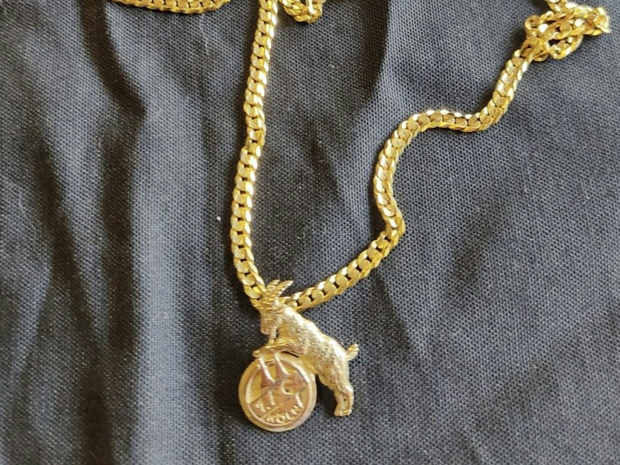 Eine goldene Kette mit dem Logo des 1. FC Köln liegt auf einem Tuch.