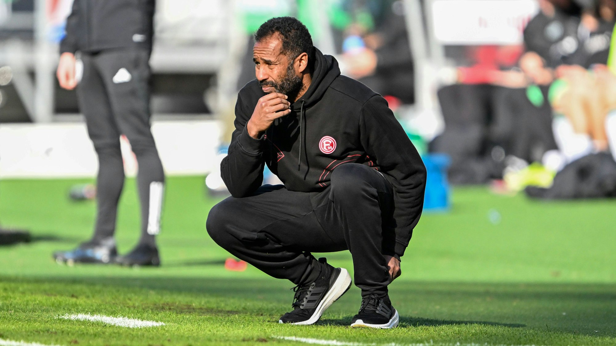 Daniel Thioune geht beim Spiel von Fortuna Düsseldorf nachdenklich in die Hocke.