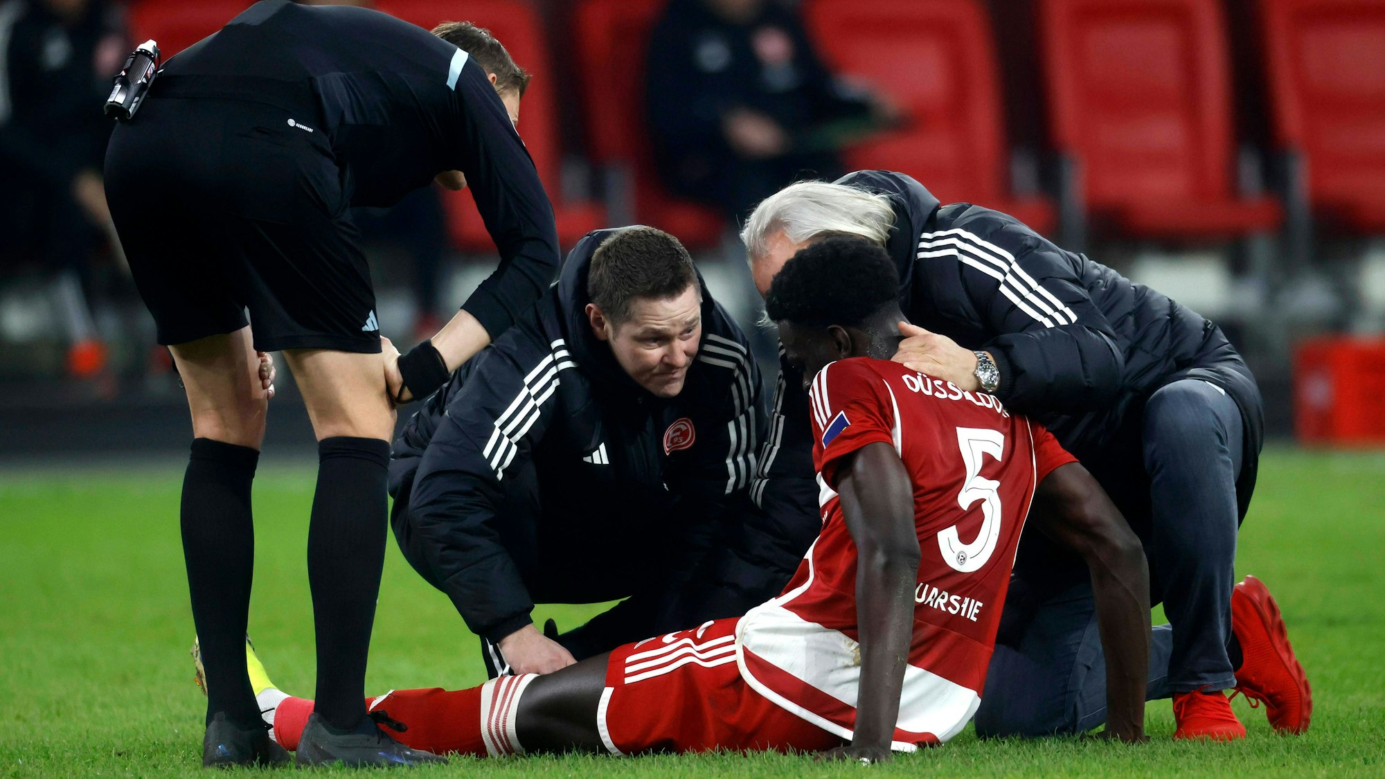 Fortuna Düsseldorfs Abwehrspieler Joshua Quarshie sitzt verletzt auf dem Platz und wird vom medizinischen Personal behandelt.