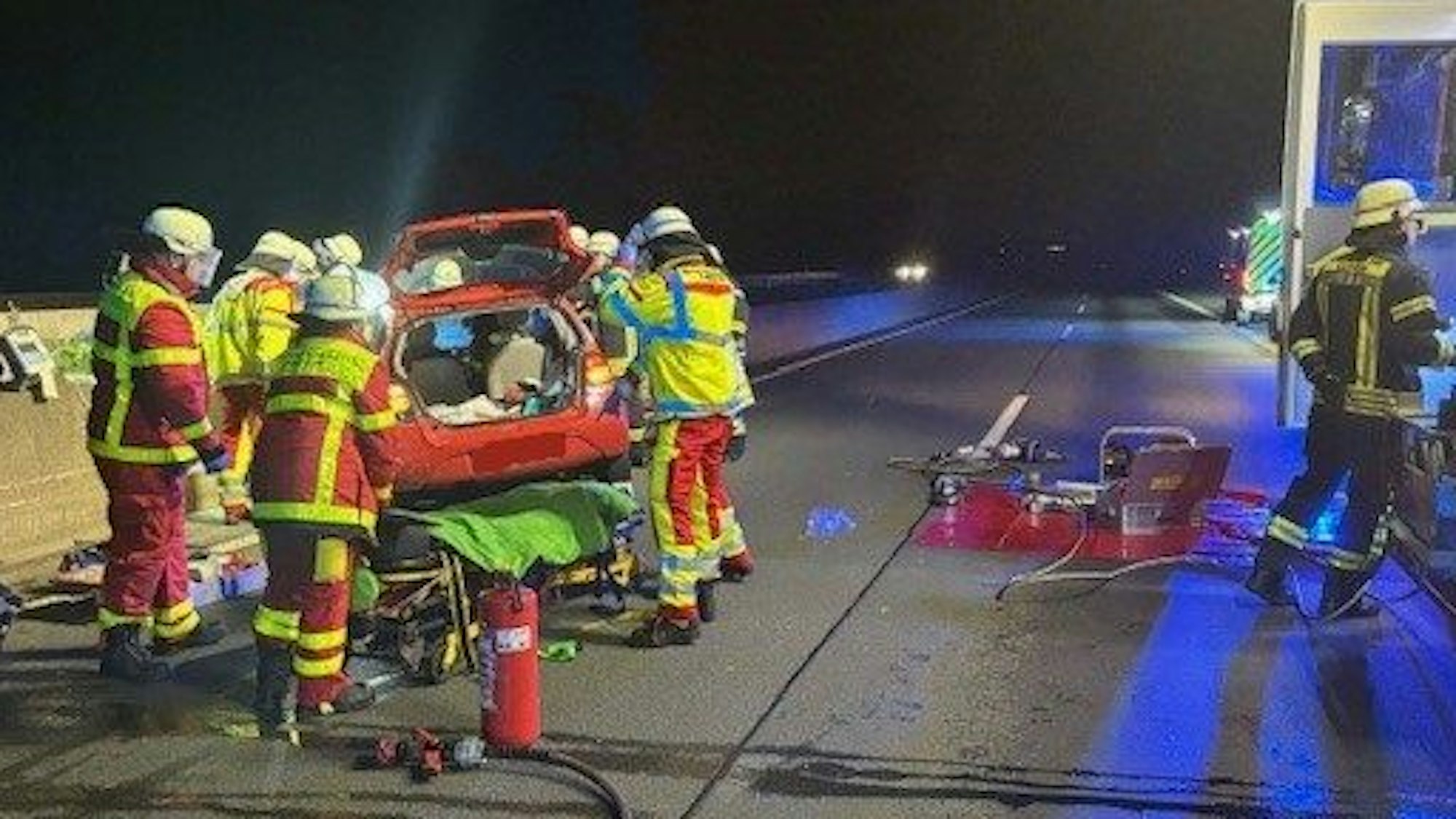 Ein Auto steht an der Betonschrammwand einer Autobahn, mehrere Einsatzkräfte der Feuerwehr versuchen, eine Person daraus zu befreien.