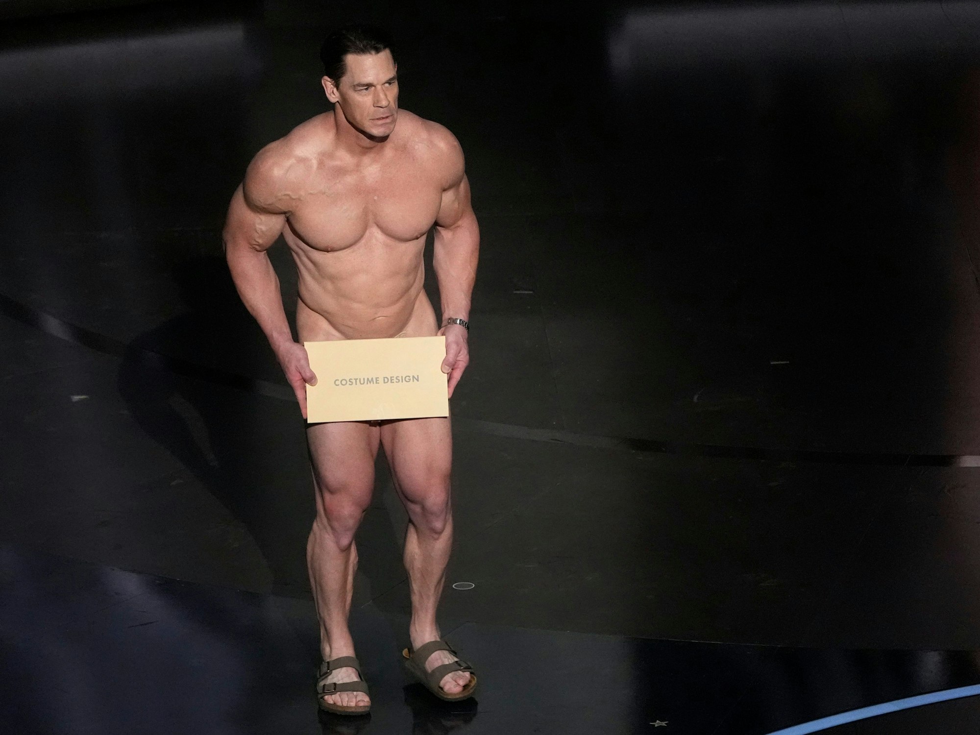 John Cena nackt auf der Bühne bei den Oscars, hält sich ein Schild vor den Intimbereich.
