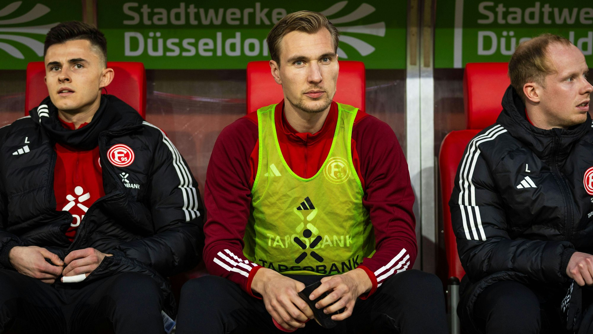 Fortuna Düsseldorfs Angreifer sitzt beim Spiel gegen den Hamburger SV auf der Ersatzbank und blickt in die Kamera.