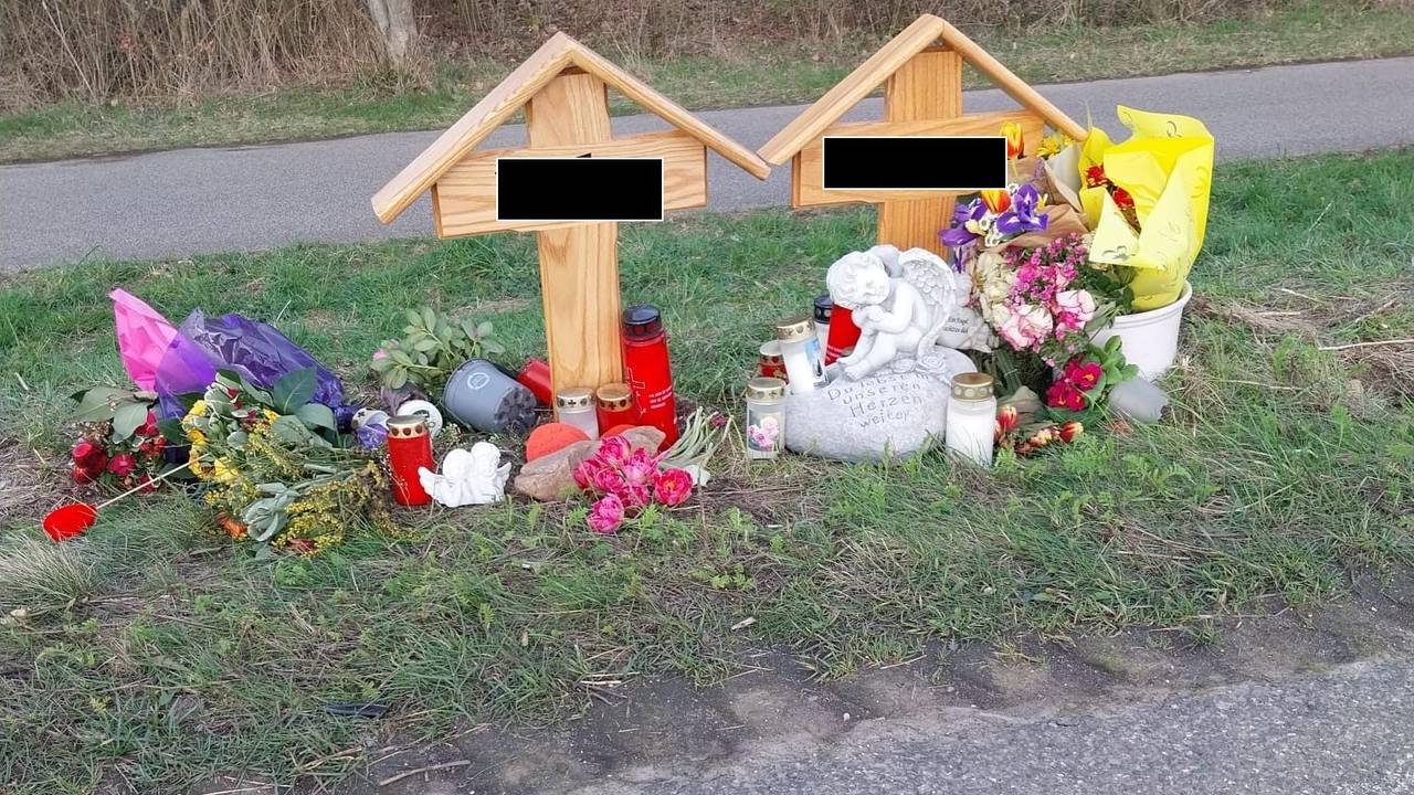 An zwei Holzkreuzen liegen Blumen, brennen Kerzen.