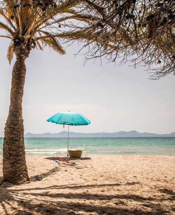 Zwei leere Stühle unter Sonnenschirmen stehen bei Sonnenschein an einem Strand.