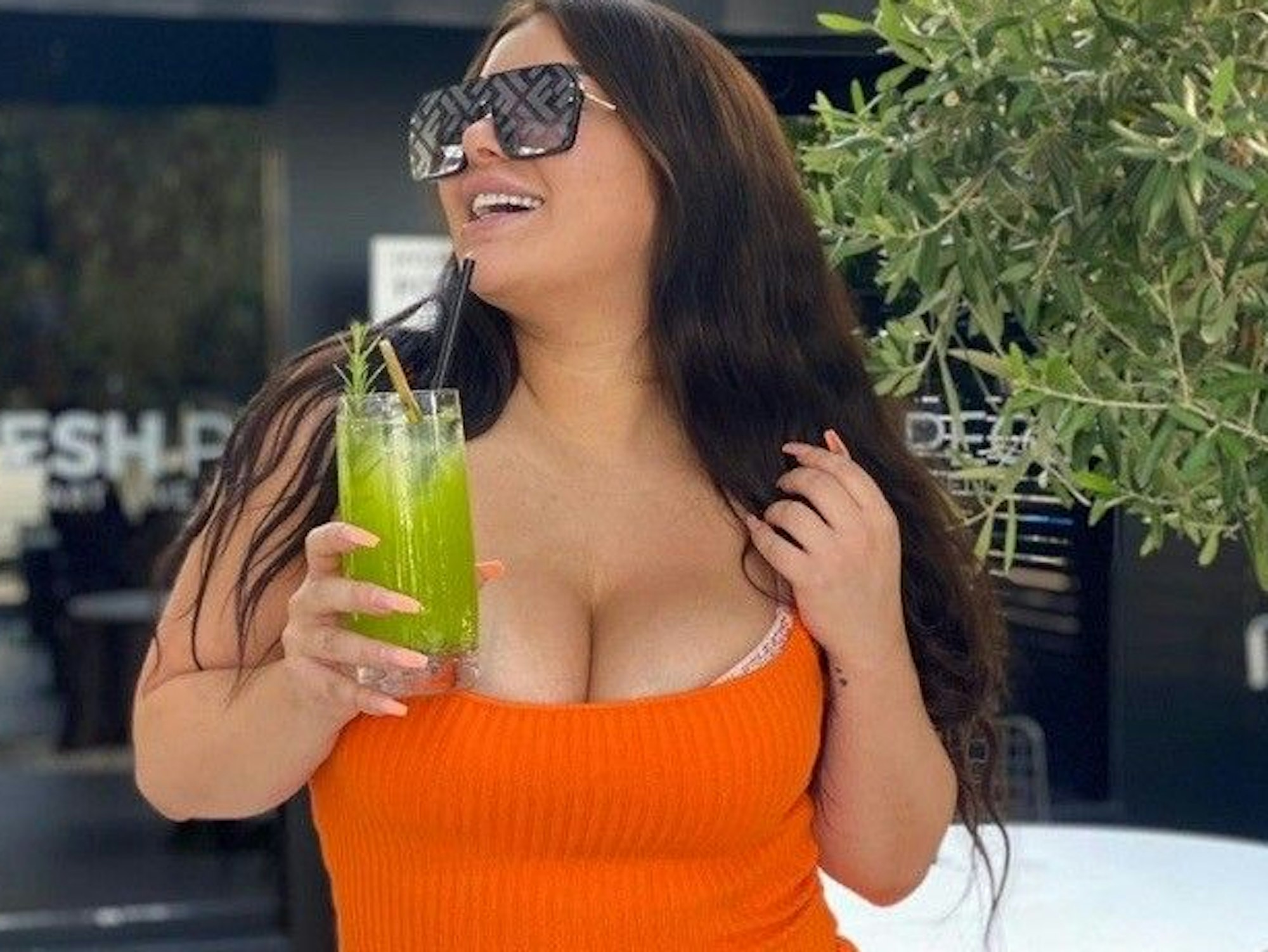 Melody Haase steht mit einem Cocktail in der Hand und einem orangen Kleid vor einer Bar.