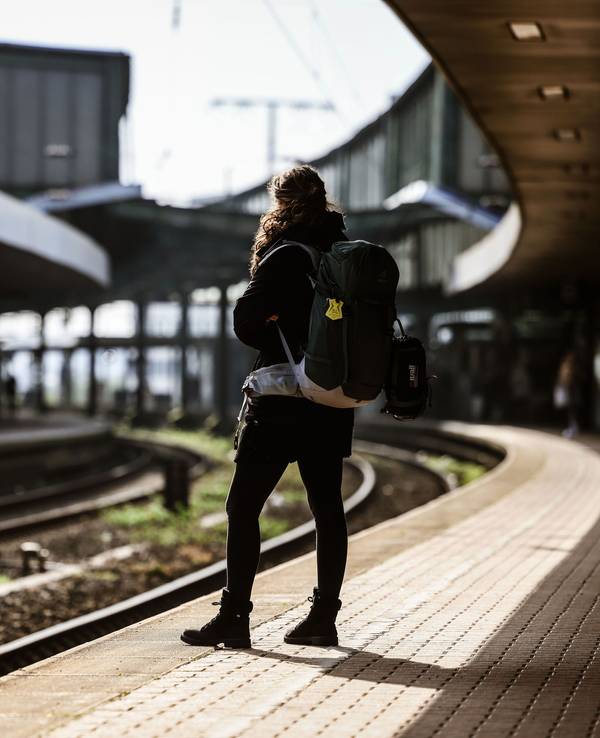 Eine Frau mit Rucksack steht auf dem Bahnsteig.