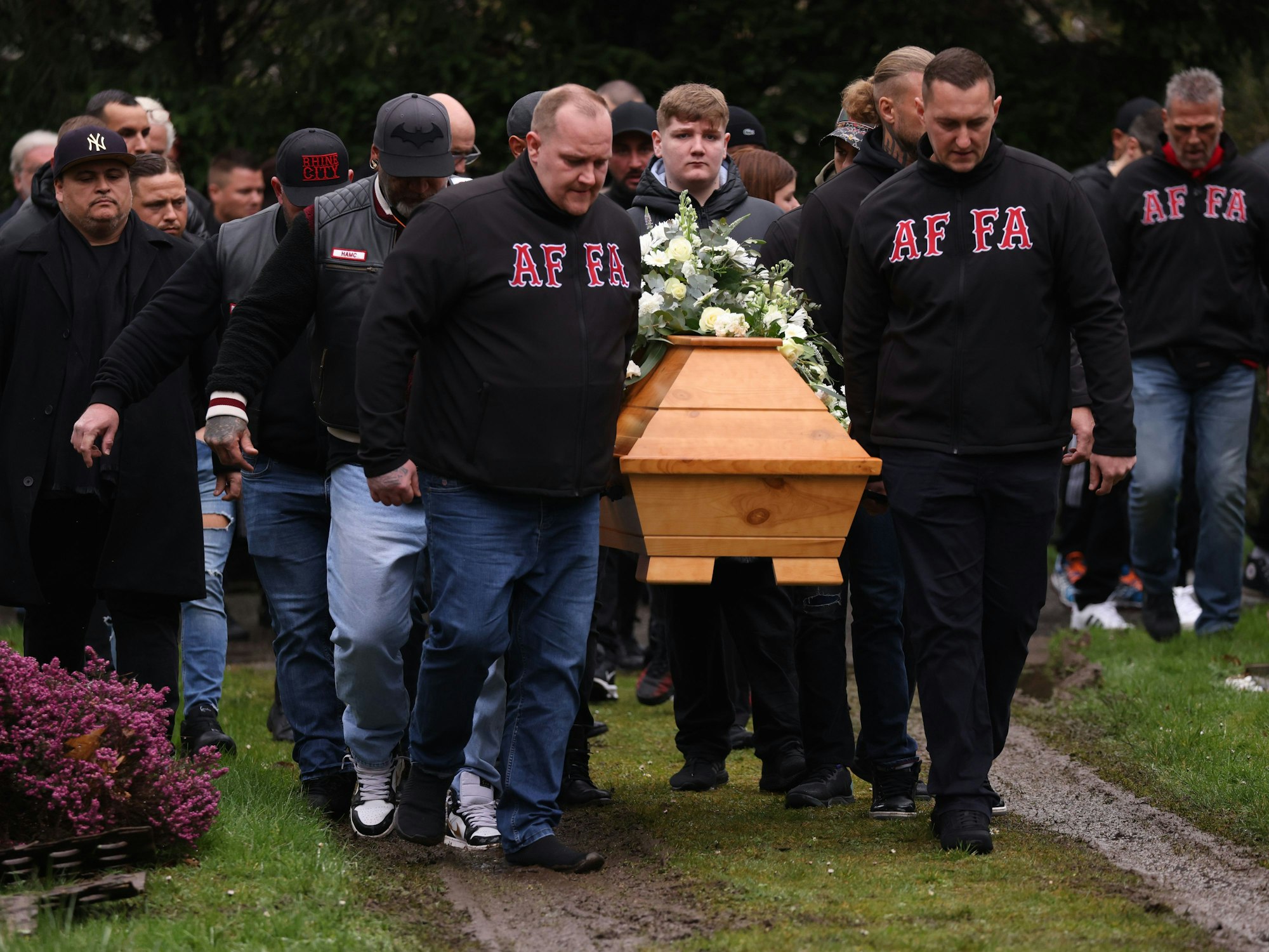 Mehrere Männer tragen einen Sarg zu einem Grab.