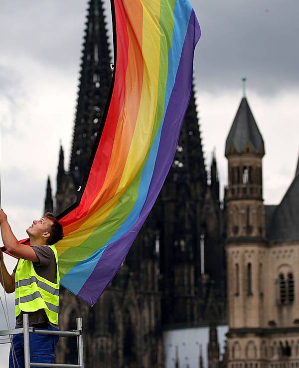 Ein Arbeiter hängt eine Regenbogenfahne vor der Kulisse des Doms und der Kirche Groß St. Martin auf.