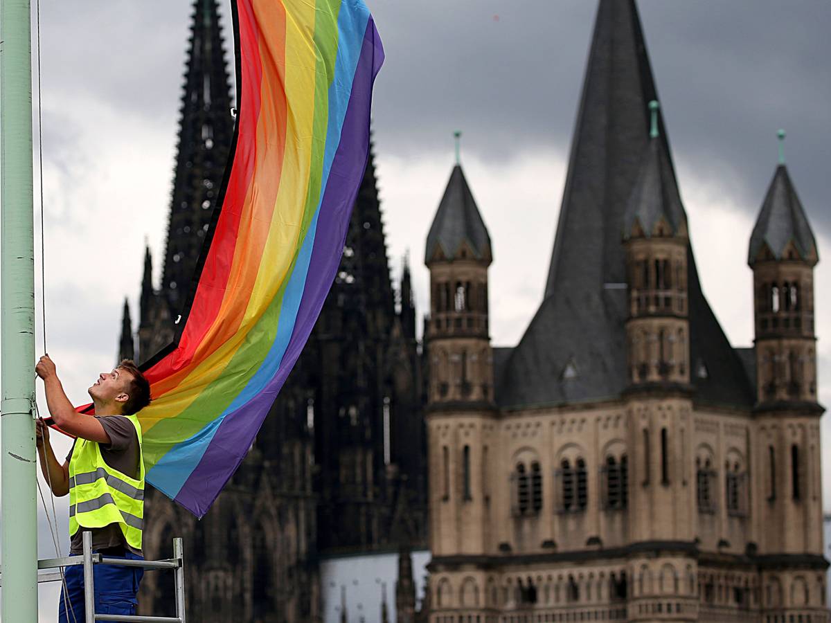 Ein Arbeiter hängt eine Regenbogenfahne vor der Kulisse des Doms und der Kirche Groß St. Martin auf.