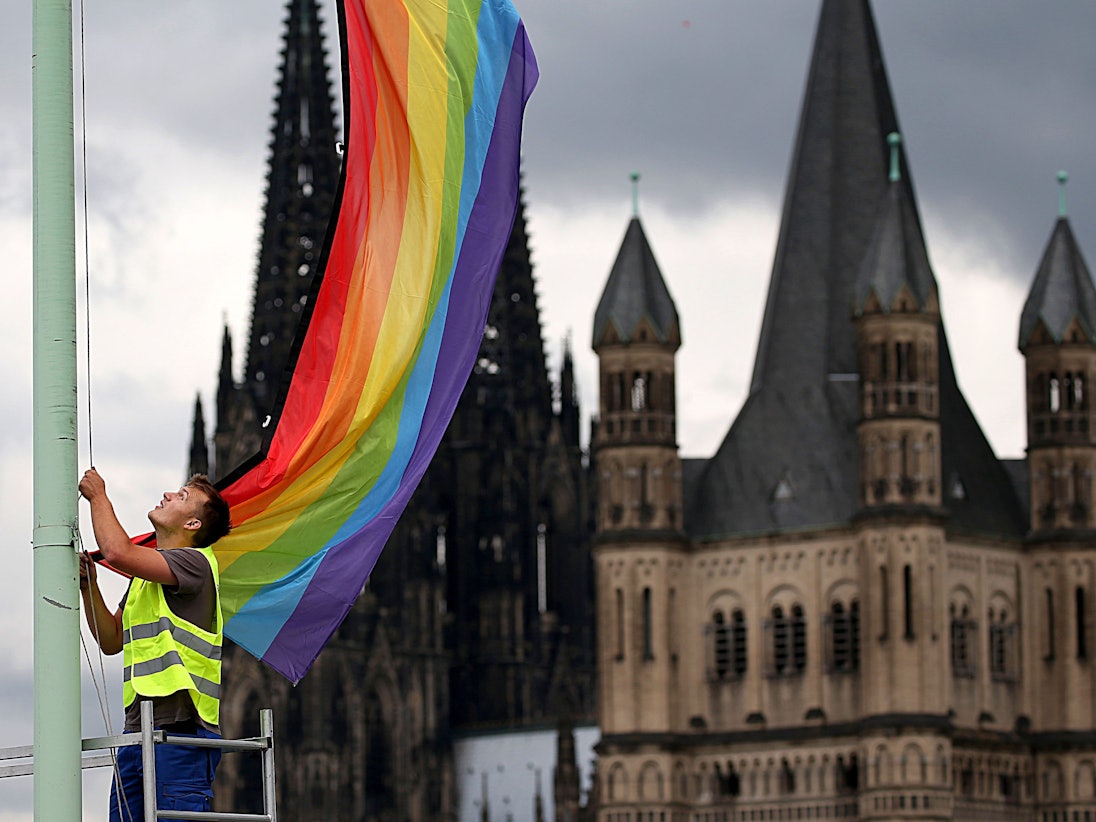 Ein Arbeiter hängt eine Regenbogenfahne vor der Kulisse des Doms und der Kirche Groß St. Martin auf.