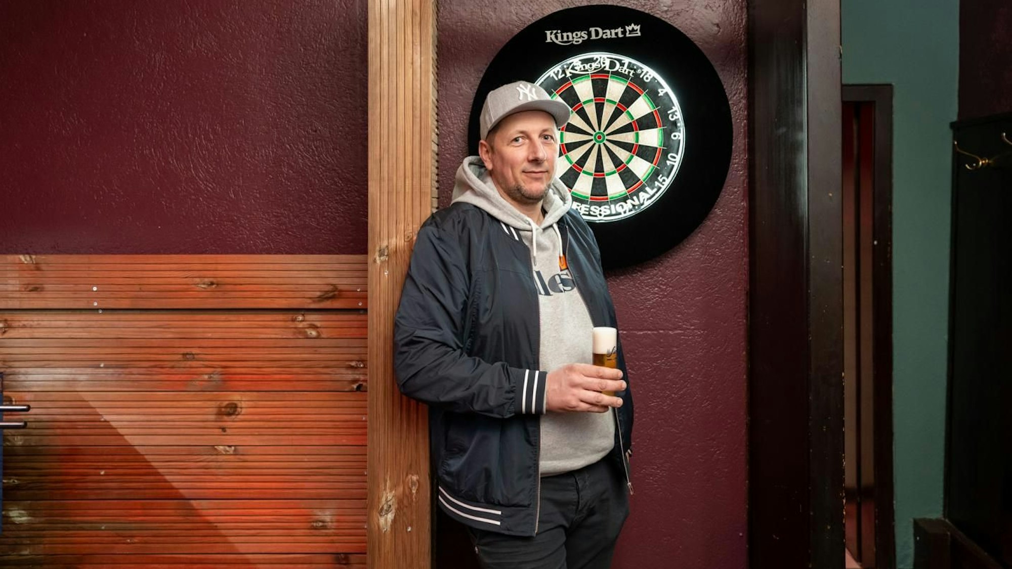 Marc Müller lehnt sich gegen die Wand und hält ein Kölsch in der Hand