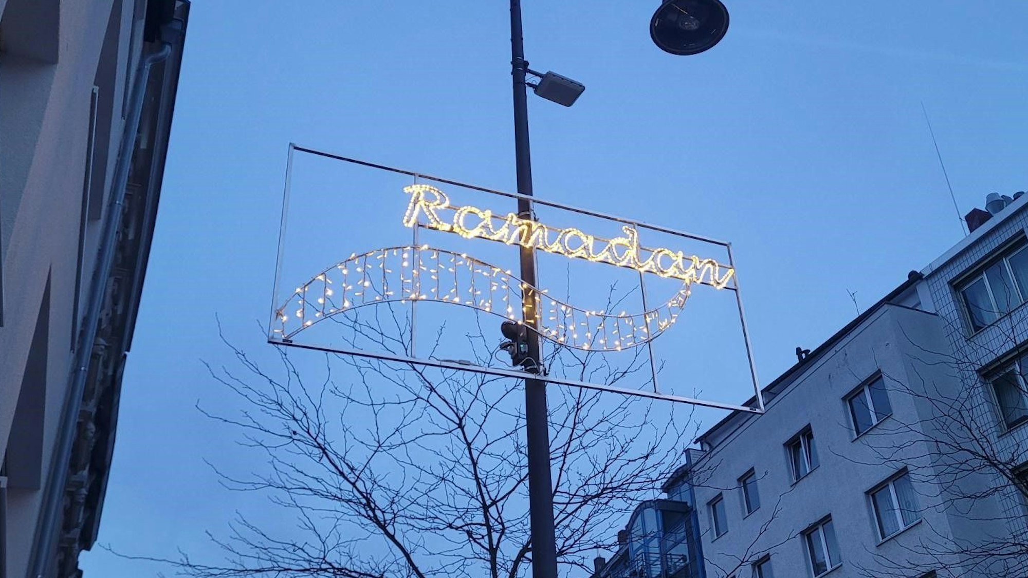 Auf der Venloer Straße fährt ein Auto, am Straßenrand ist die Ramadan-Beleuchtung zu erkennen.