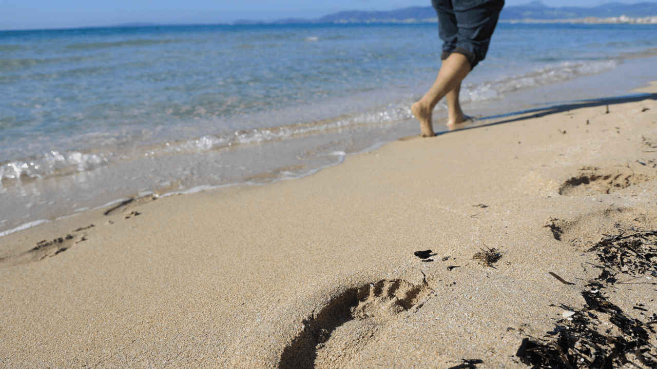 Ein Mann geht barfuß am Strand spazieren.