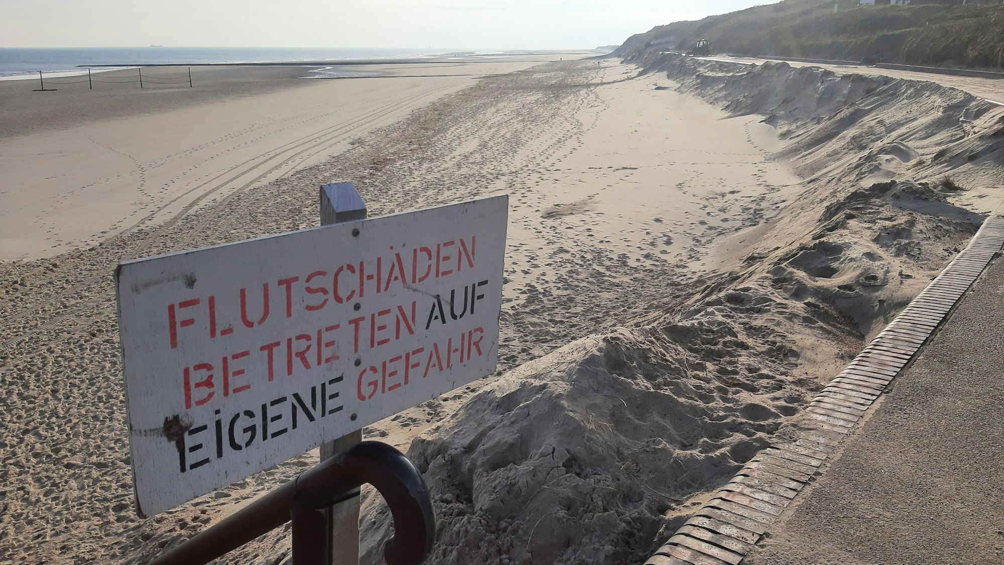 Ein Schild mit der Aufschrift „Flutschäden, Betreten auf eigene Gefahr“ steht am Strand.