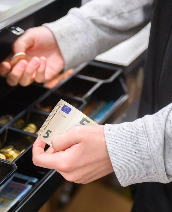 Eine Kassiererin nimmt Wechselgeld aus der Kasse eines Supermarktes.