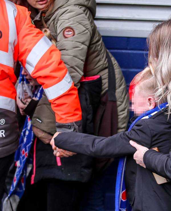 Ein am Kopf verletztes Kind wird von einem Ordner an der Hand aus dem Stadion geführt. Von hinten hält eine Frau das Kind fest.