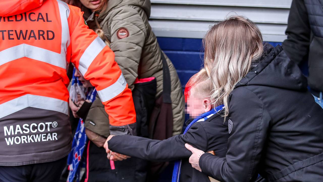 Ein am Kopf verletztes Kind wird von einem Ordner an der Hand aus dem Stadion geführt. Von hinten hält eine Frau das Kind fest.