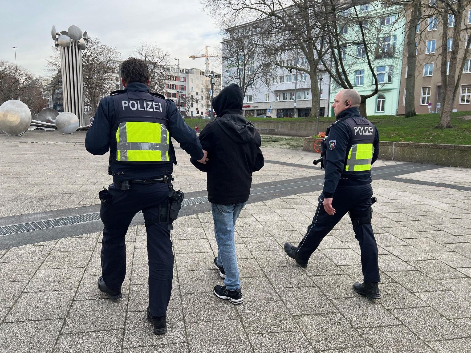 Ein Polizist führt einen Jugendlichen am Arm über einen Platz, ein zweiter Polizist läuft nebenher.