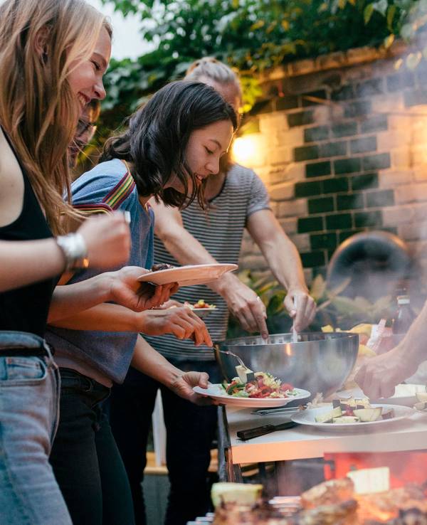 A young group of friends are helping themselves to freshly prepared food at a summer evening Barbecue.
