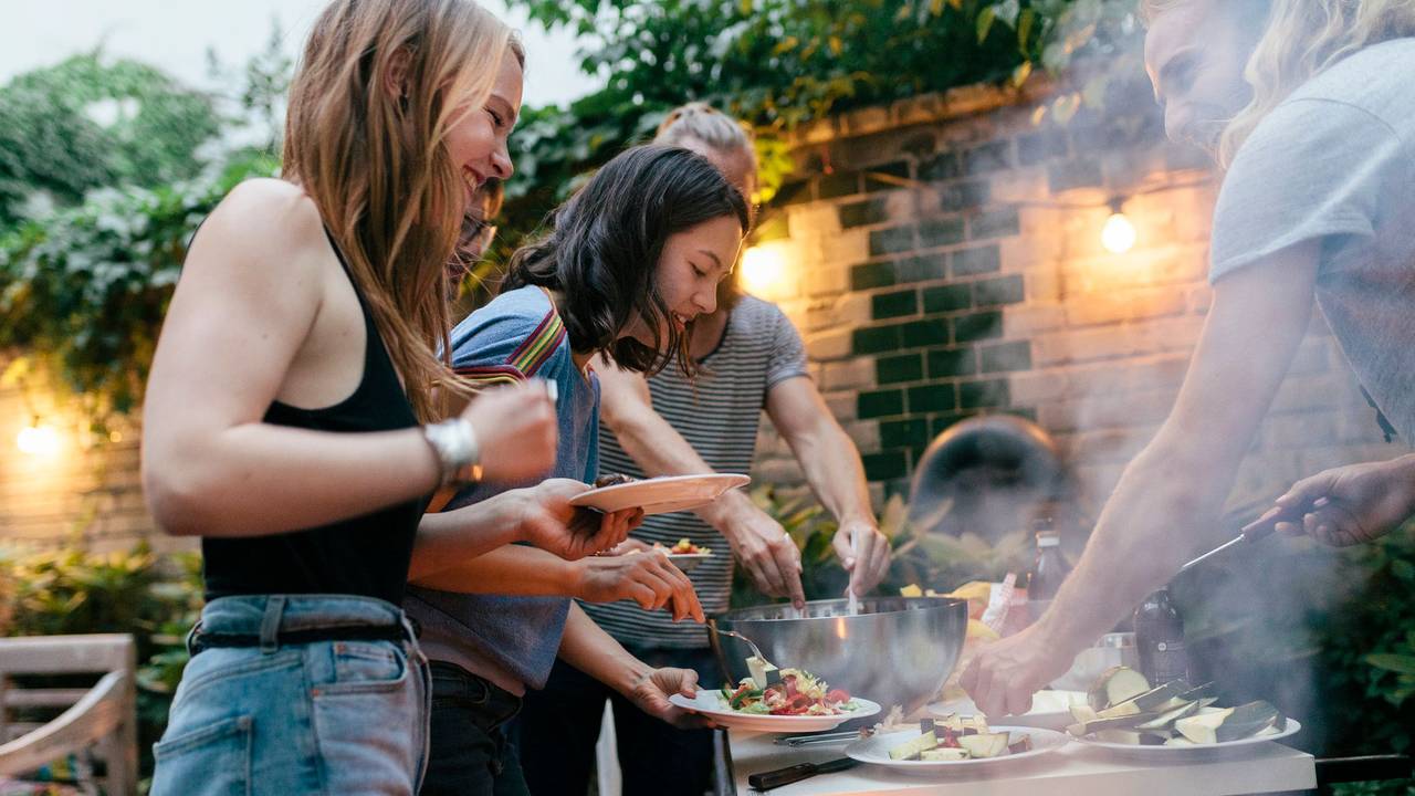 A young group of friends are helping themselves to freshly prepared food at a summer evening Barbecue.