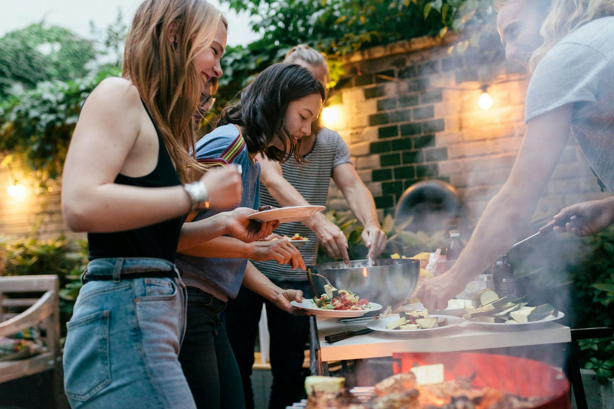 A young group of friends are helping themselves to freshly prepared food at a summer evening Barbecue.