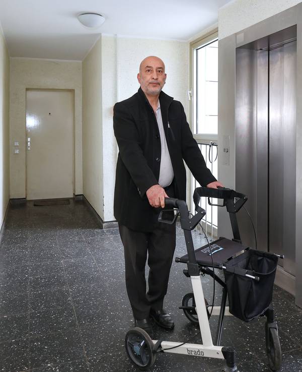 Ein Mann steht mit einem Rollator vor einem Aufzug.