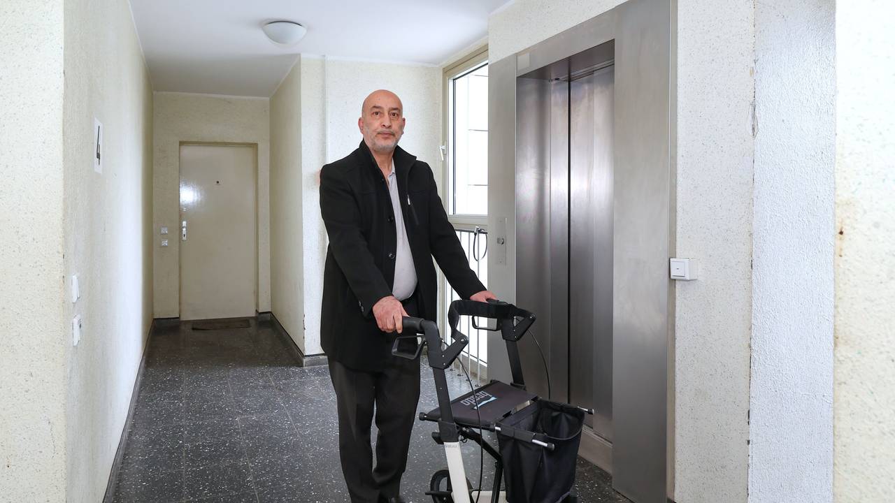 Ein Mann steht mit einem Rollator vor einem Aufzug.