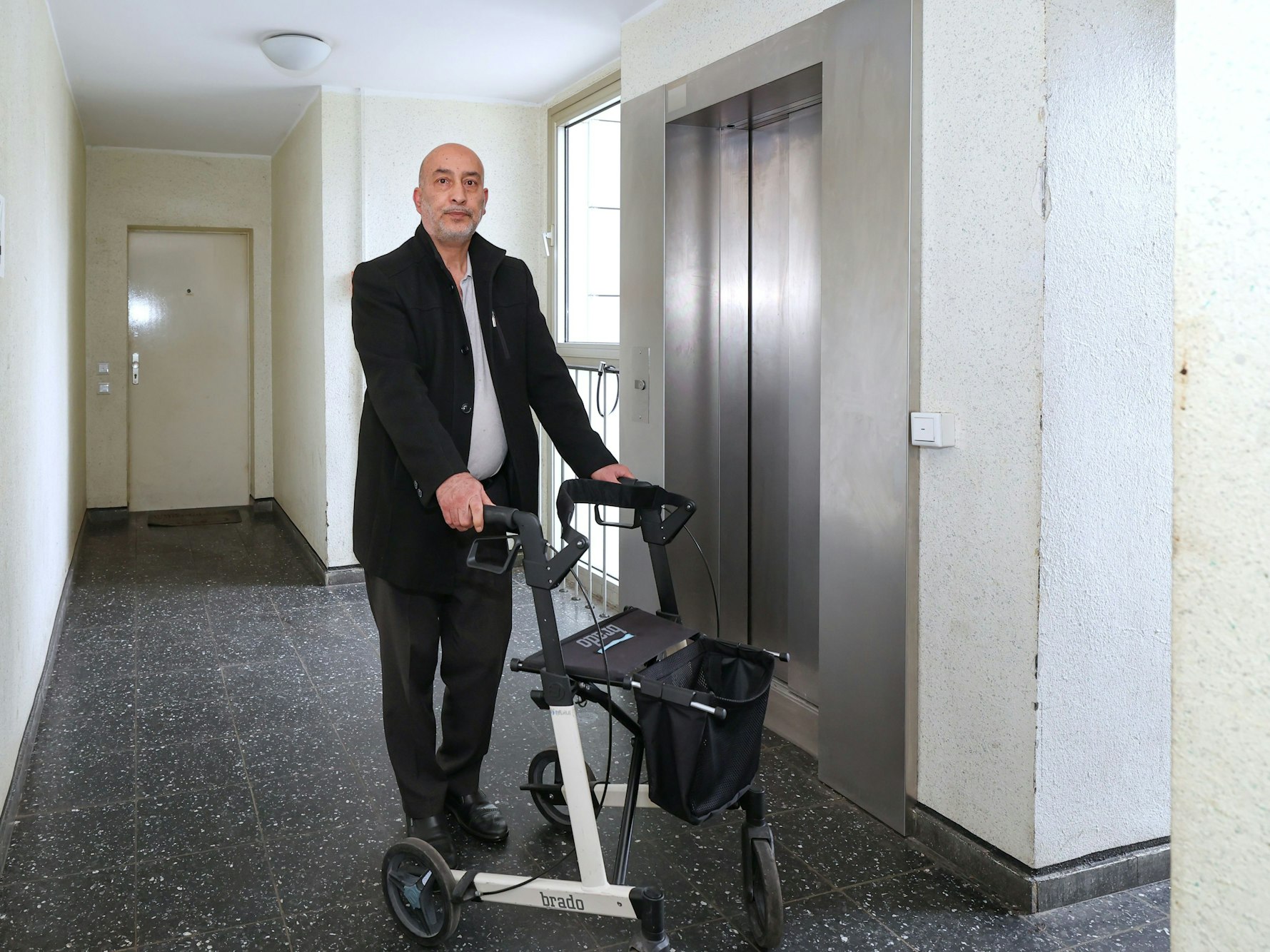 Ein Mann steht mit einem Rollator vor einem Aufzug.