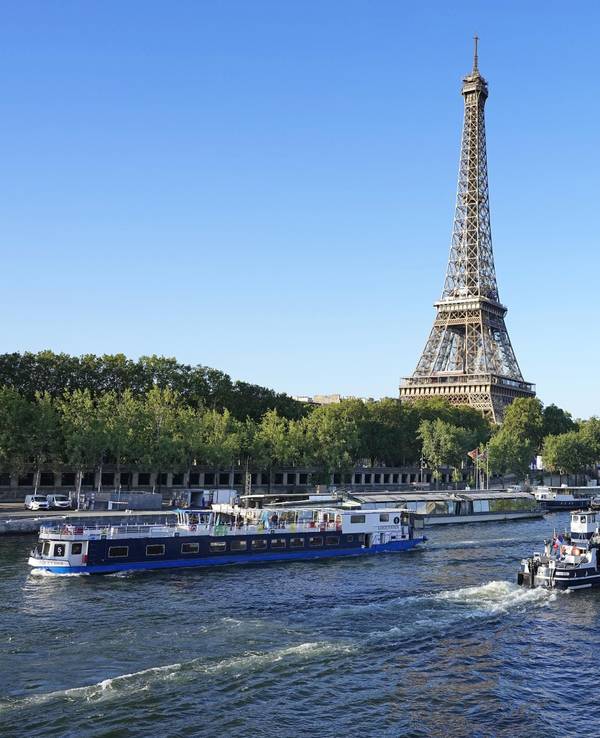 Ein Boot und ein Lastkahn fahren vor dem Eiffelturm auf der Seine während eines Tests für die Eröffnungsfeier der Olympischen Spiele 2024 in Paris. Für die Eröffnungsfeier der Spiele am 26. Juli 2024 sind Tausende von Olympioniken auf rund 160 Booten auf dem Fluss geplant.