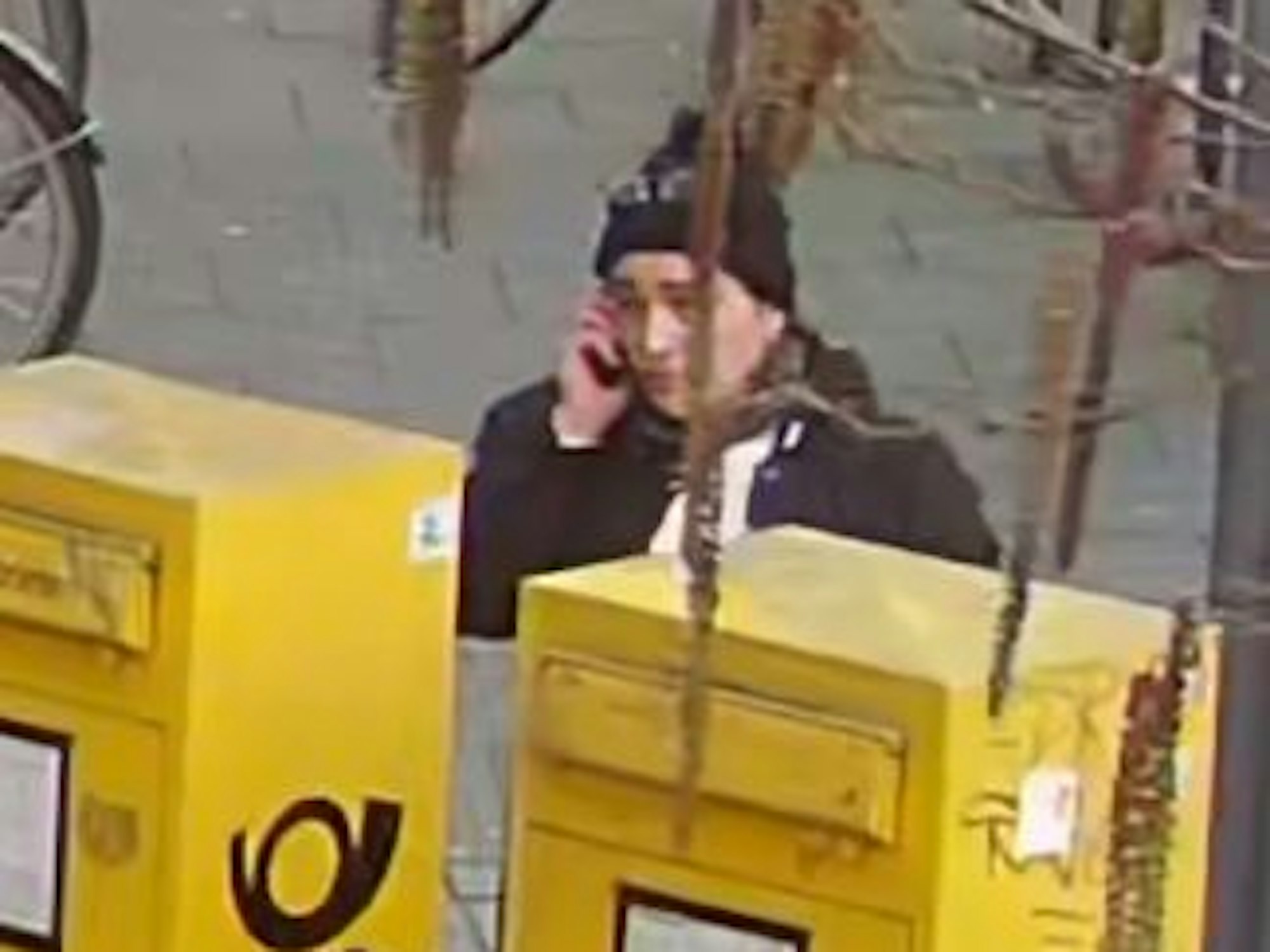 Mutmaßliche Betrügerin steht an Postkästen in Köln und telefoniert mit dem Handy.