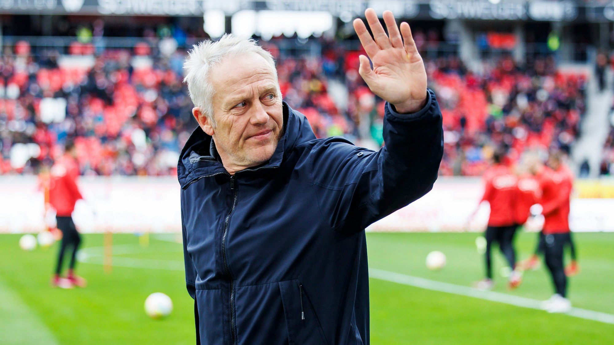 Christian Streich winkt vor einem Spiel des SC Freiburg in die Zuschauerränge.