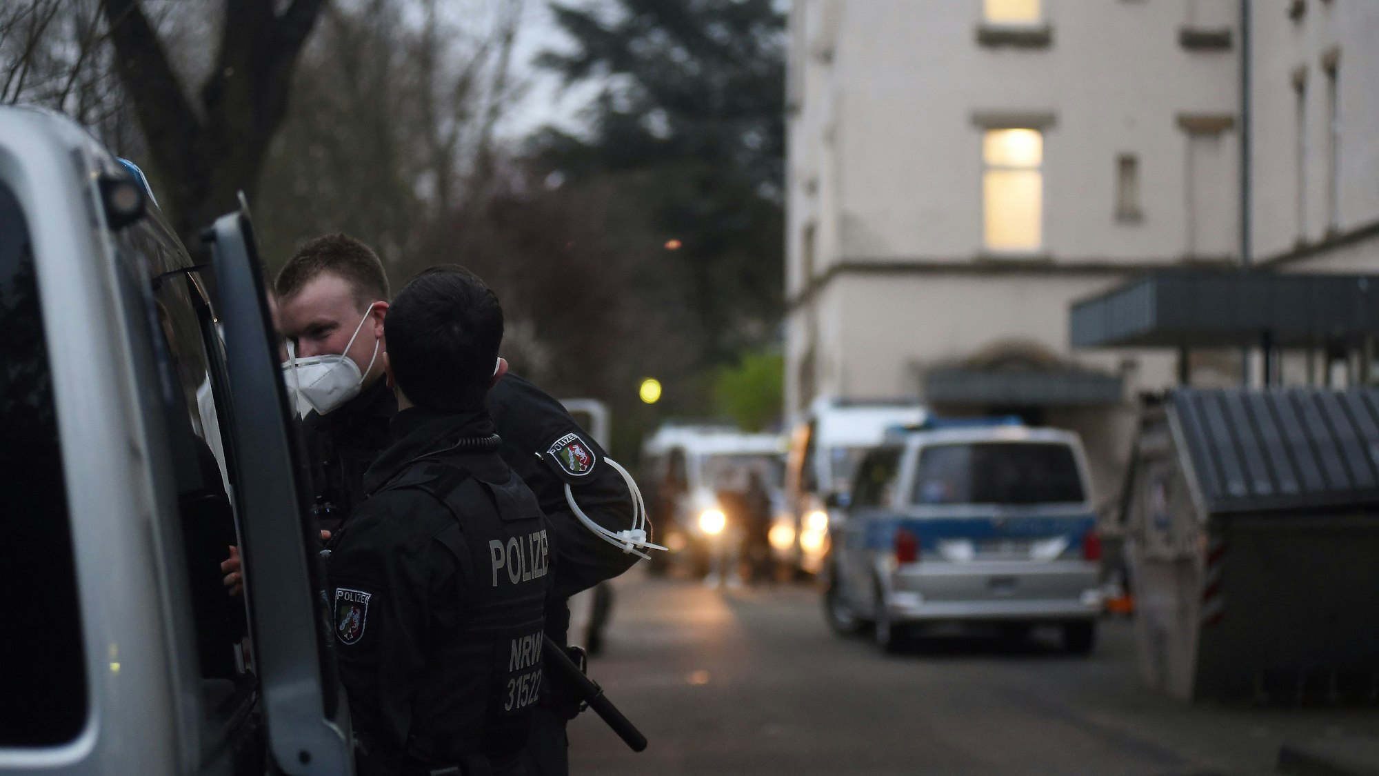 Polizisten stehen vor einem großen Haus bei einer Razzia.