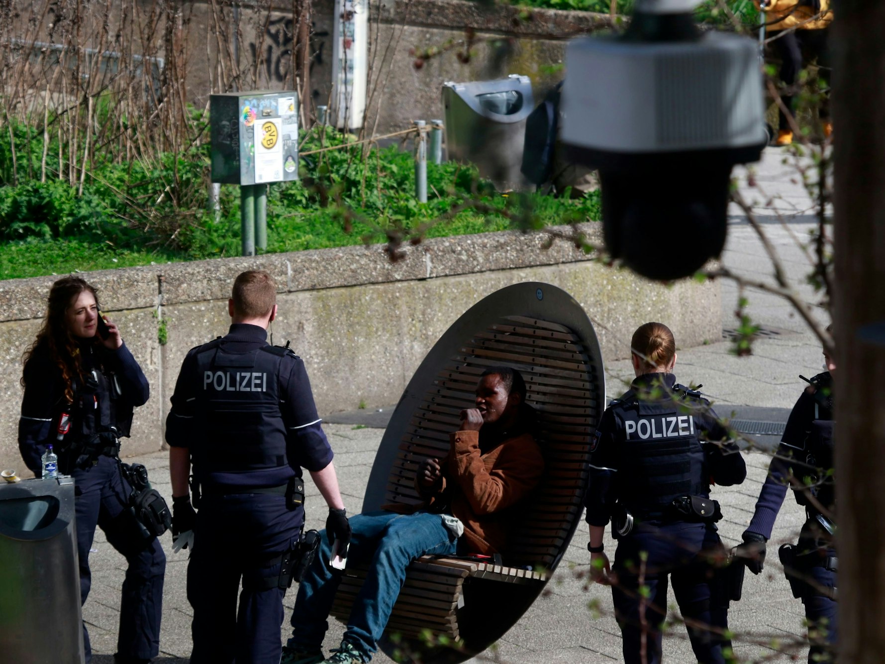 Ein Mann sitzt am Ebertplatz, drei Einsatzkräfte der Polizei stehen vor und neben ihm.